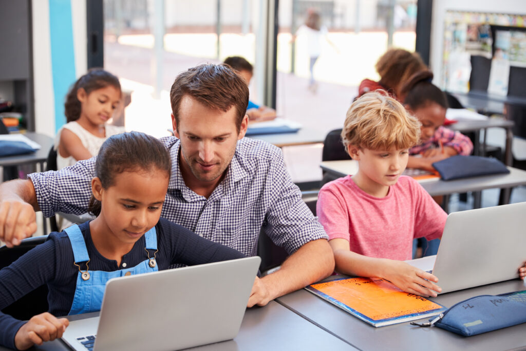 Teacher Helping Young Students Using Laptops In Class