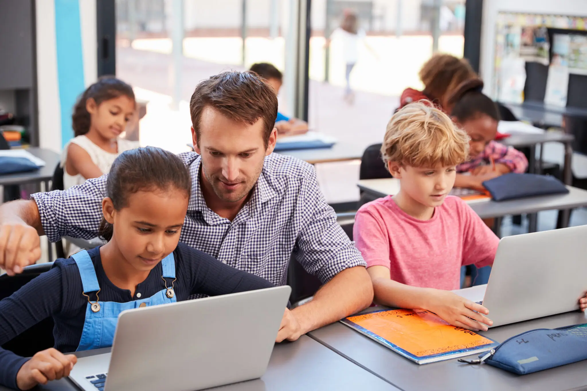 A Teacher helps young students use their laptops in class.