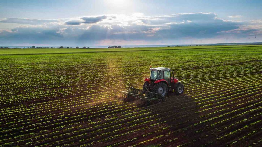 A tractor plows farmland with the sun rising in the background.
