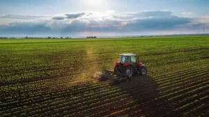 A tractor plows farmland with the sun rising in the background.