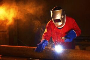 A man in protective welding equipment welds a steel pole.