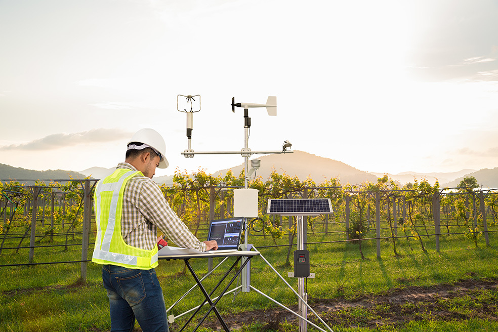 Person with a hard hat on operating weather data instruments in a field