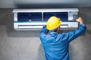 A technician in a hard hat works on an A/C unit.
