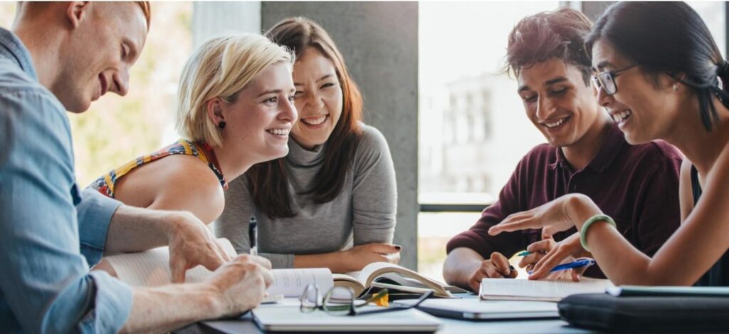 A group of young people sit around a table chatting.