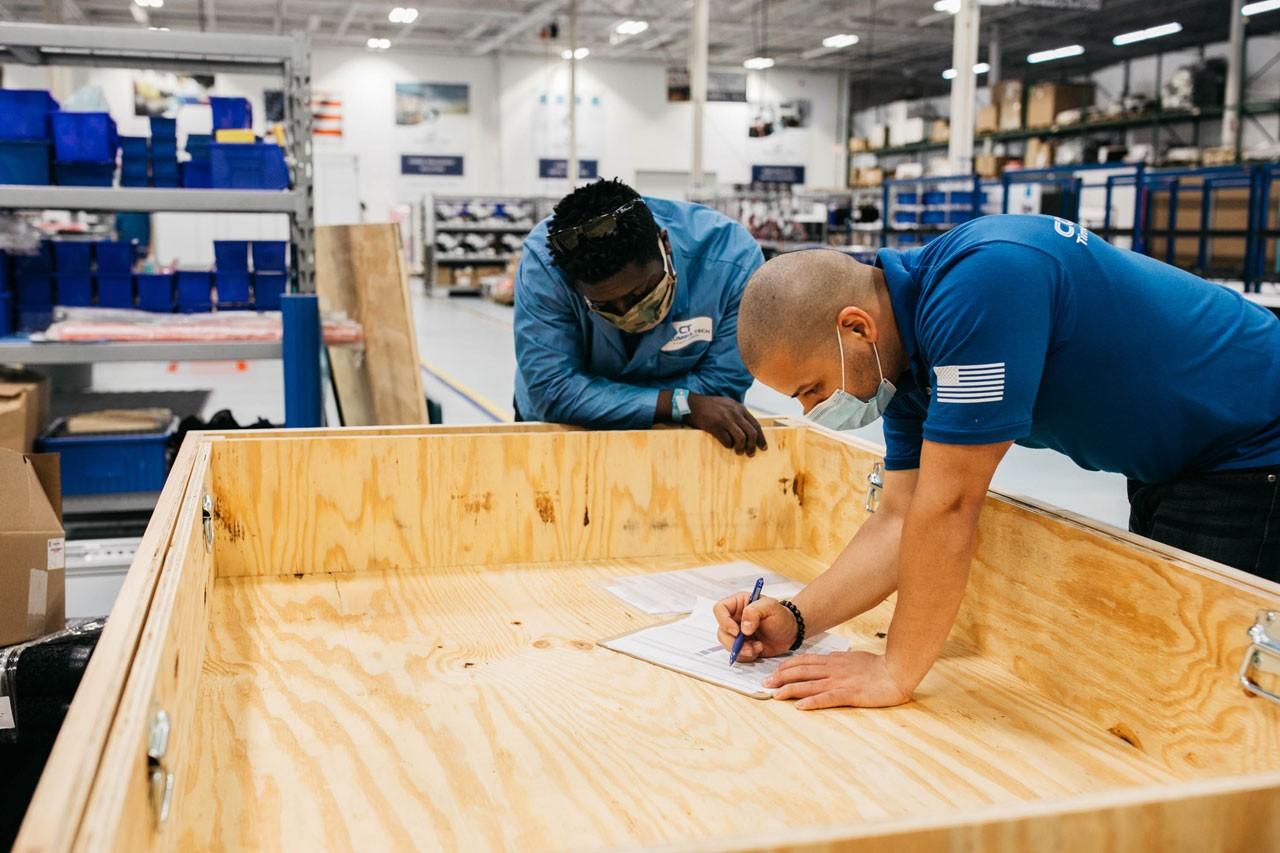 Blog 42 Two workers stand over a wooden desk writing notes on a sheet of paper.