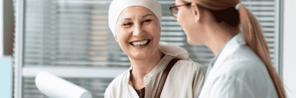 A woman wearing a head wrapping smiles while talking with a doctor.