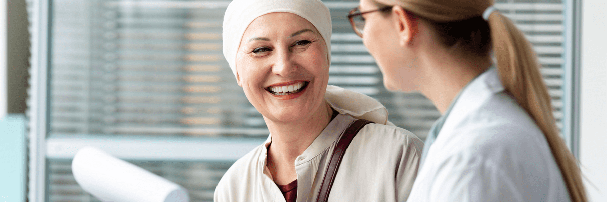 Blog 32 A woman wearing a head wrapping smiles while talking with a doctor.