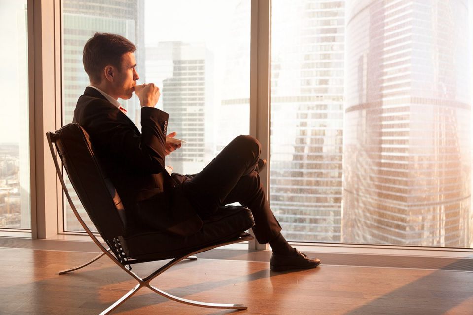 Blog 53 A businessman sits in a chair and contemplatively looks out the window of an office.