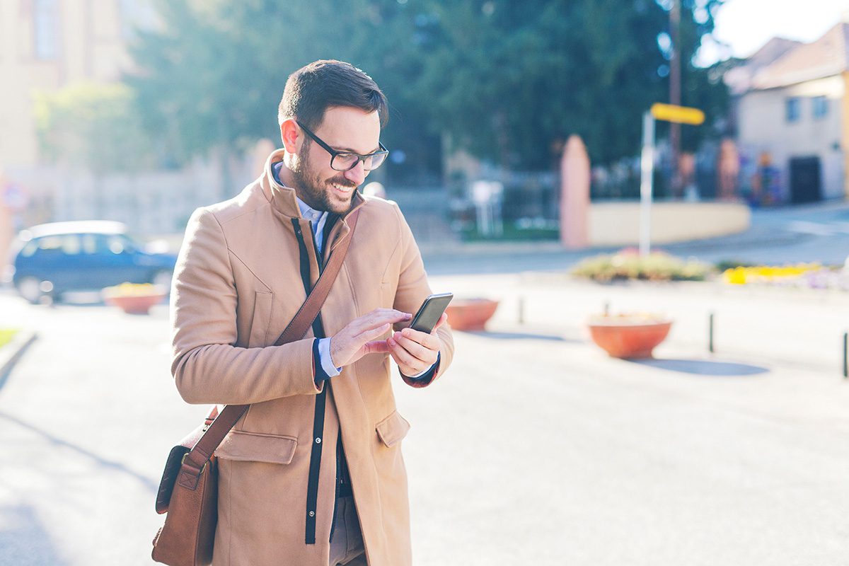 Handsome man looking at the phone while walking down the street