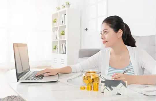 A young woman sits at a desk, working on a laptop and taking notes.