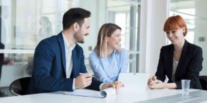 Three people in business attire smile while talking at a table.