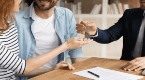 Trois personnes sont assises autour d’une table basse. L’une d’elles remet un trousseau de clés à une autre