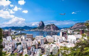 A plane flies over the Rio De Janeiro skyline in daytime.