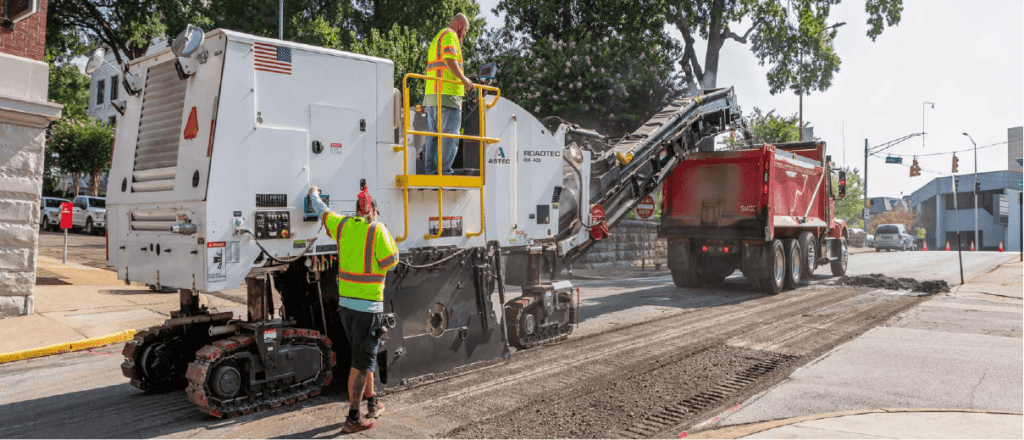 A man operates a large machine on the street, engaged in construction or maintenance work.