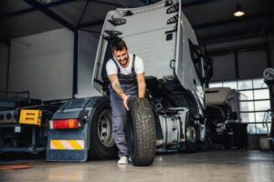 A mechanic in overalls rolls a tire away from the cab of an 18-wheeler.