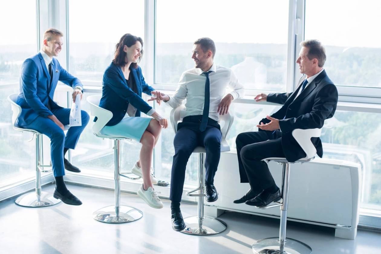 Four business people sit in a semi-circle discussing with each other.