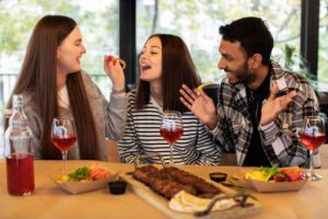 Three friends enjoying a meal and wine together at a restaurant, sharing laughter and good conversation.