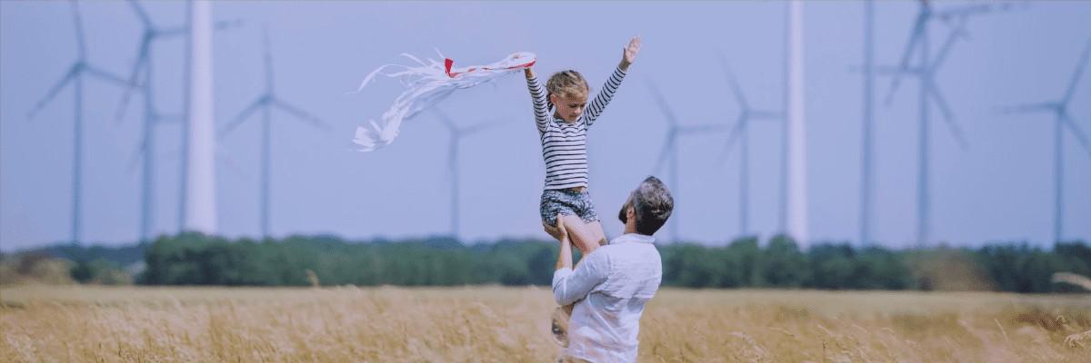 Father lifts child in the air with windmills in the background.