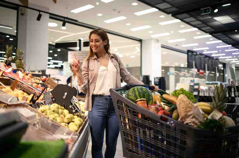 A smiling woman shops in the produce section of a grocery store.