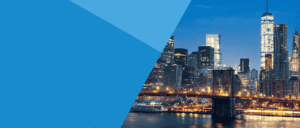 The New York City skyline at dusk features illuminated skyscrapers, the Brooklyn Bridge with glowing lights, and reflections on the calm East River.