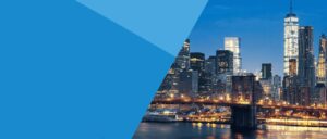 The New York City skyline at dusk features illuminated skyscrapers, the Brooklyn Bridge with glowing lights, and reflections on the calm East River.