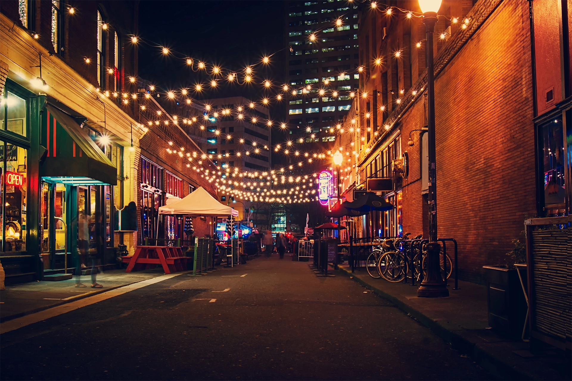 Blog 27 A city alleyway at night lit up with string lights, connecting buildings like Hire2Retire connects Infor HCM to Google Workspace.