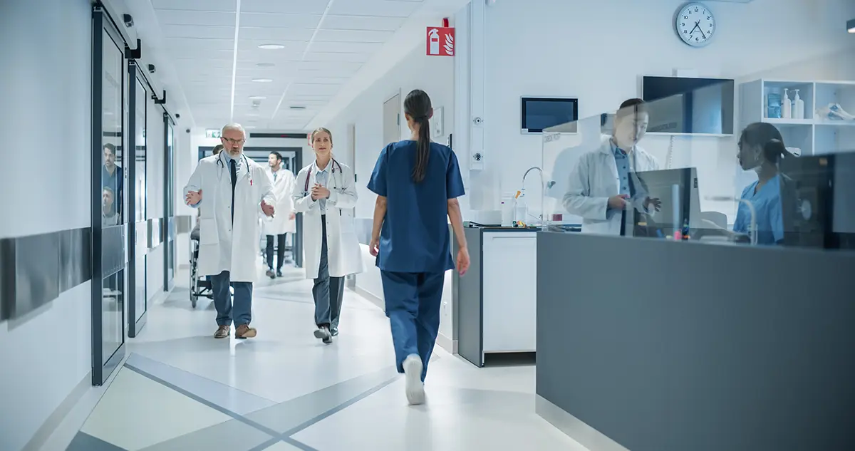 Blog 17 Diverse Male and Female Medical Professionals Navigate a Busy Hospital Corridor and Registration Area, Having Conversations About Healthcare, they use Hire2retire for Identity management