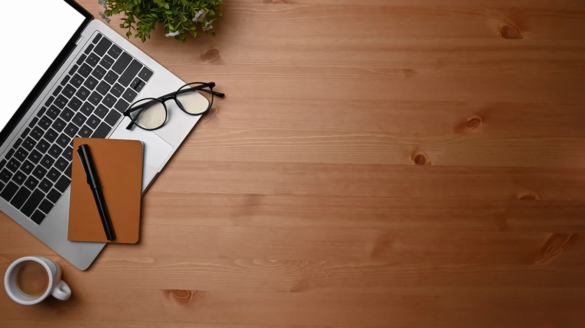 How To Homepage 26 An overhead view of a wooden office desk, with a laptop and glasses in the top left corner.