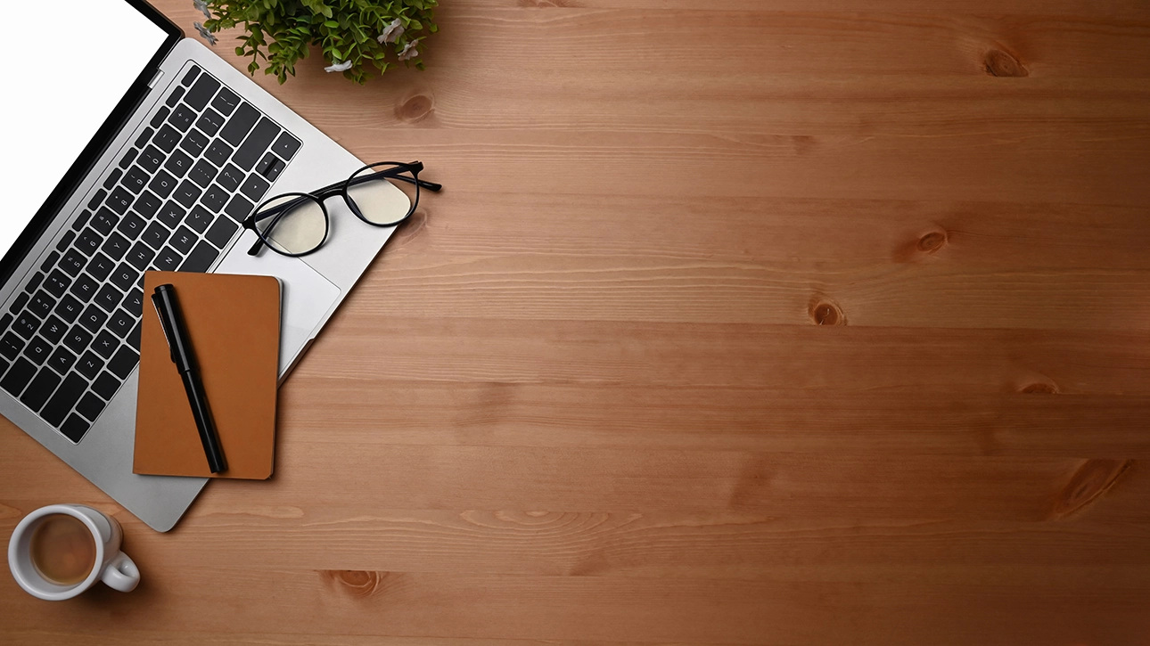 Hire2Retire Phase 8.6: OneDrive Reassignment on leave, Skillsoft support, & more 1 An overhead view of a wooden office desk, with a laptop and glasses in the top left corner.
