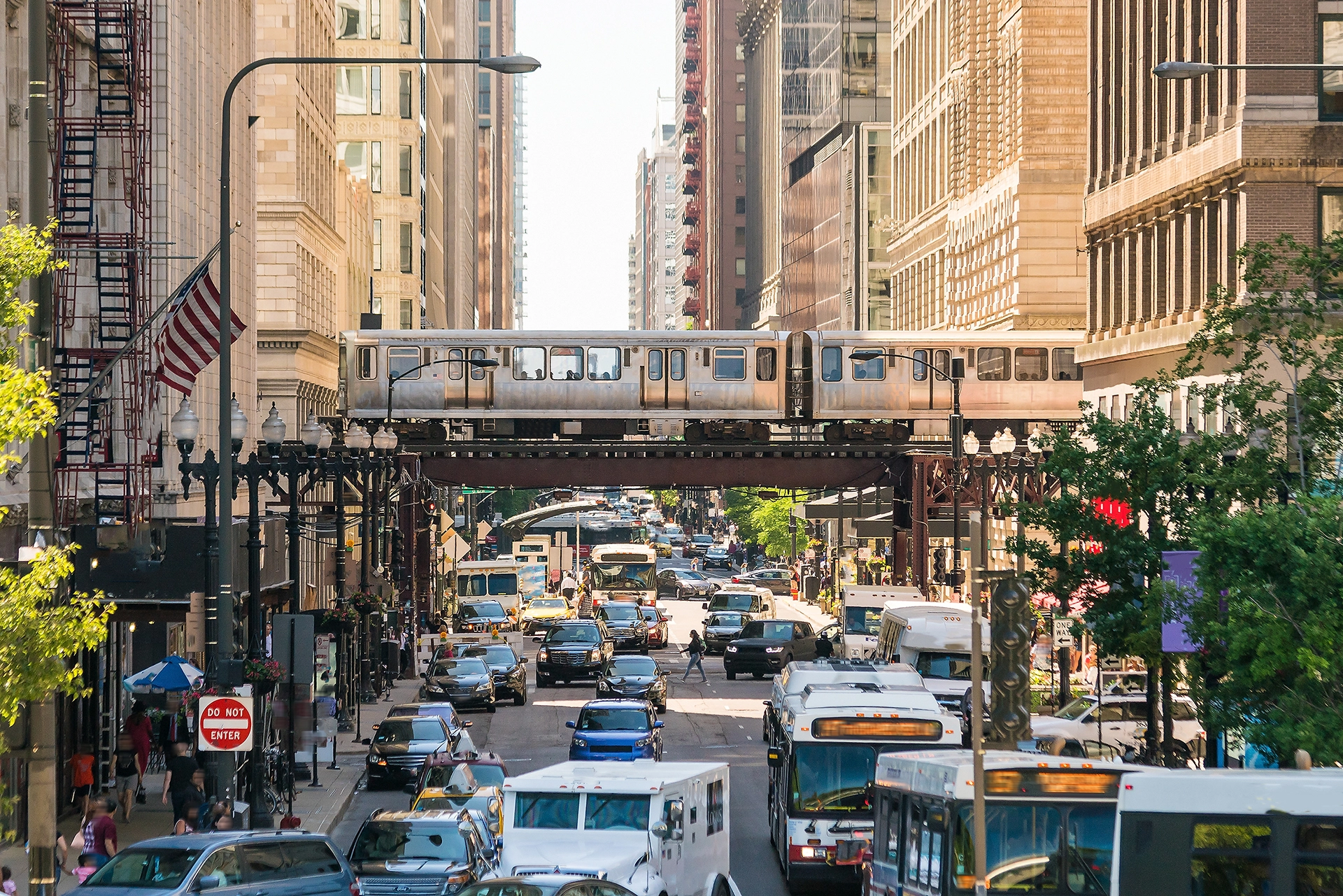 Blog 21 Cars and trucks drive down a busy downtown city street. A passenger train travels above them.