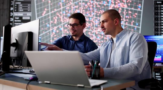 Two men in business attire evaluate data security measures and delete employee profiles on a laptop.