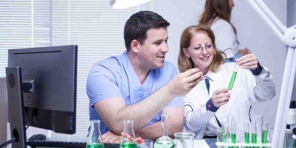 Smiling scientist colleagues in their uniform sitting in chimical lab.