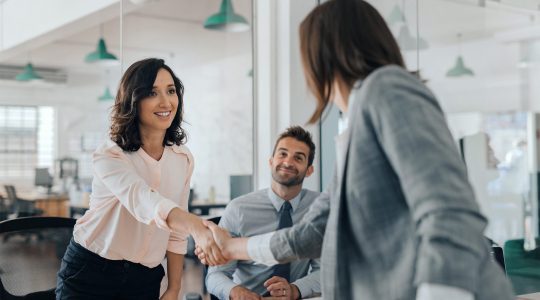 Smiling young woman, and shaking hands with a co-worker, the organization uses Oracle HCM as their HR system.