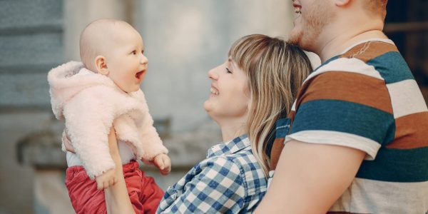 A mother and father smile at a baby who is smiling back at them.