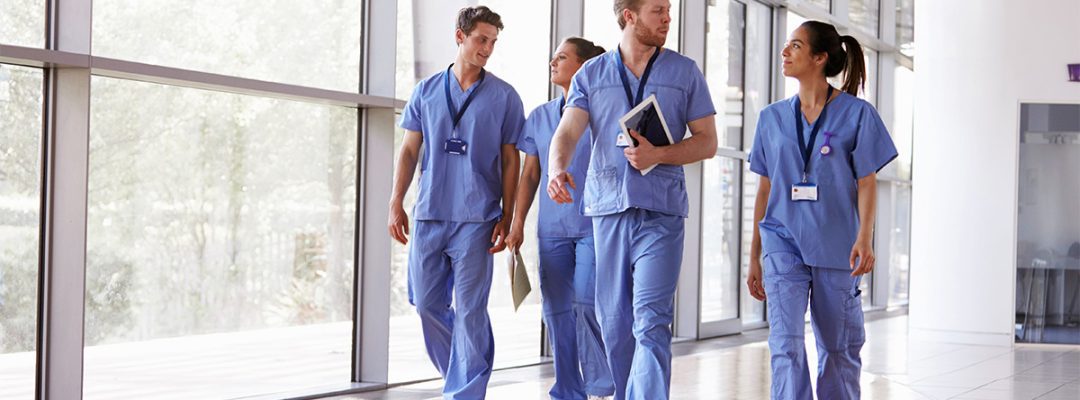 Four healthcare workers in scrubs walk down a hallway