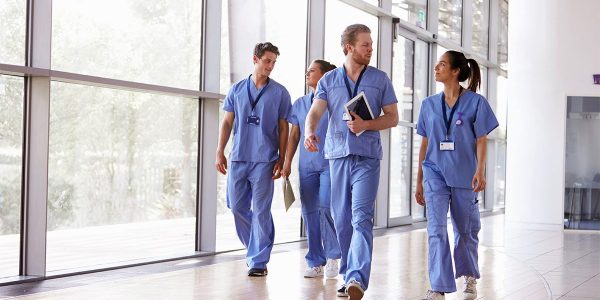 Four healthcare workers in scrubs walk down a hallway.