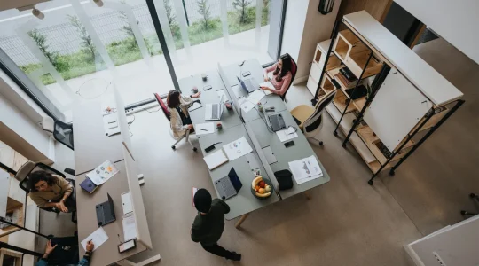 An overhead view of employees working at a desk in an office. Their company uses Hire2Retire’s PayMaster integration for employee onboarding automation.