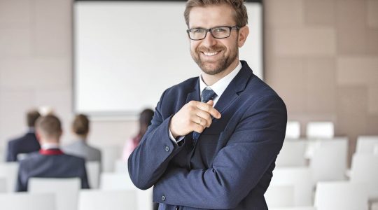 Portrait of happy businessman standing in seminar hall using Hire2Retire