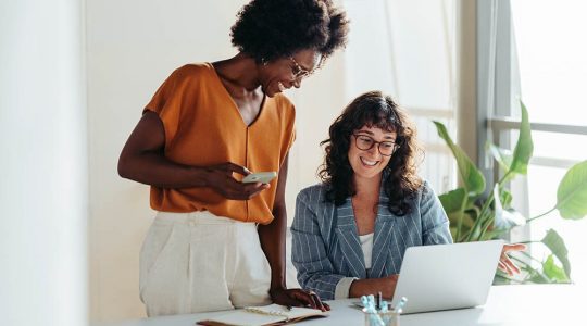 Two female entrepreneurs using a laptop for a productive business meeting in a corporate workplace.
